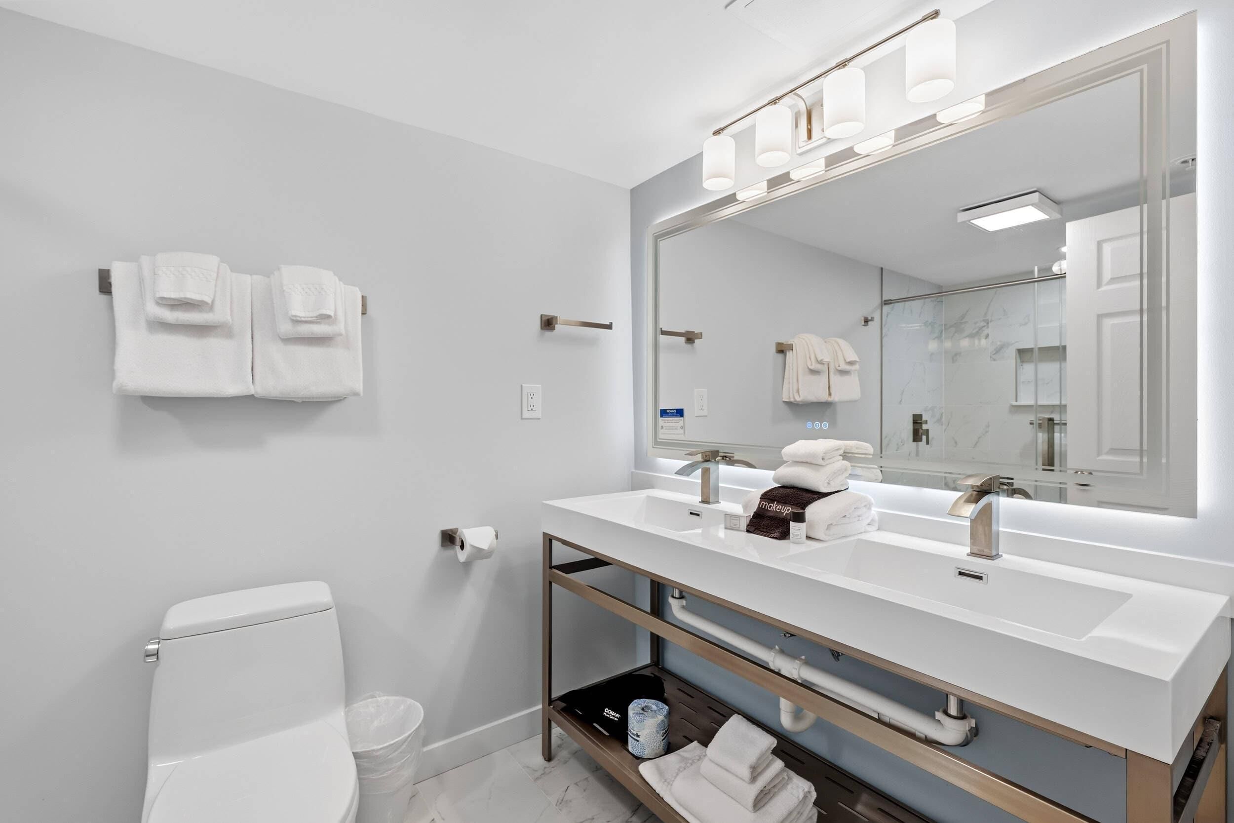 A modern bathroom with a white sink, a large mirror, and two towel racks.
