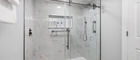 A modern bathroom with a glass-enclosed shower, marble tiles, and a towel rack.
