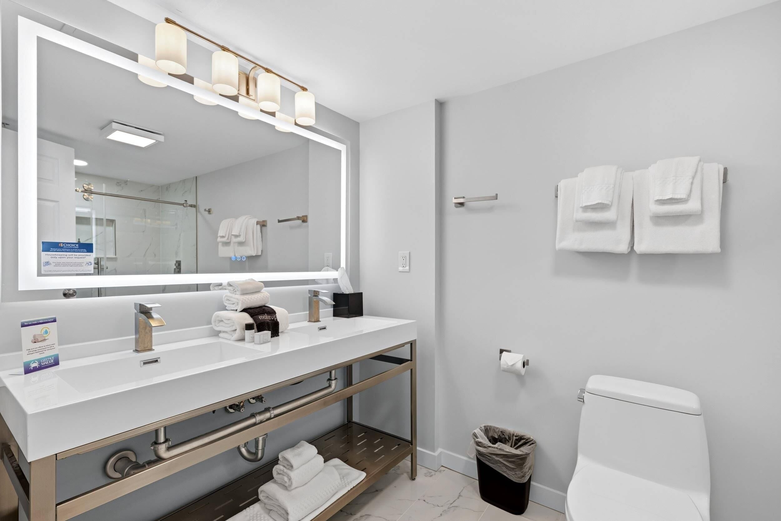 A modern bathroom with a large mirror, dual sinks, a vanity, and a toilet.