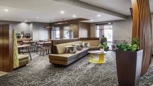 A modern hotel lobby with a seating area, a coffee station, and a large planter with plants. - SpringHill Suites Tempe at Arizona Mills Mall (Tempe)