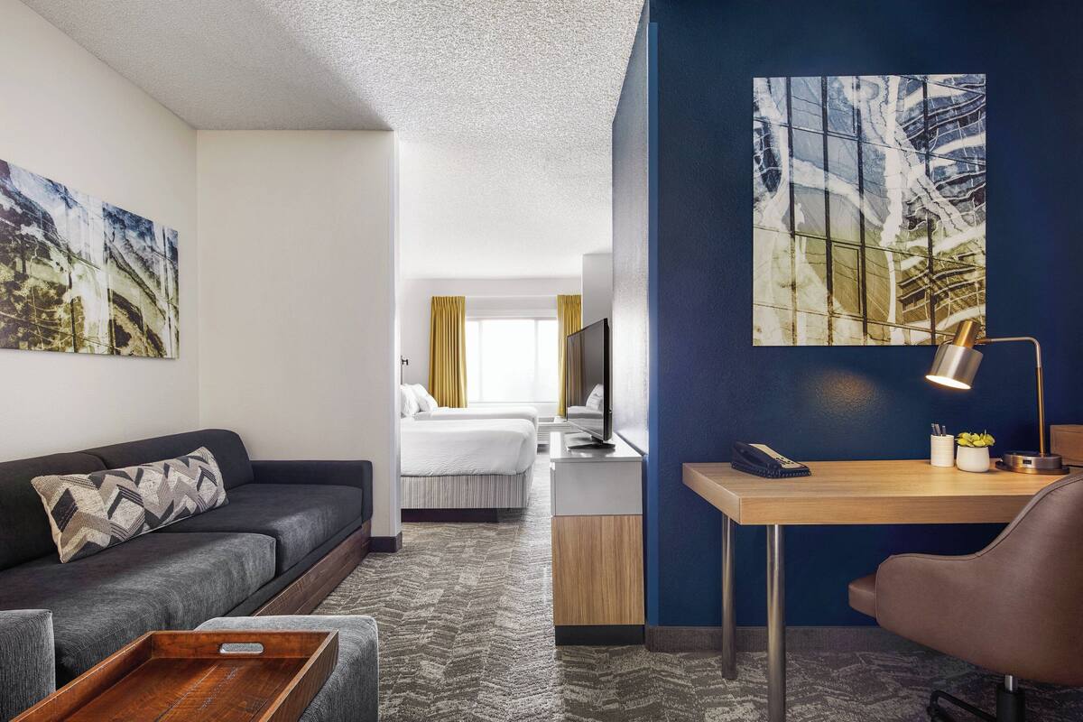 Une chambre d’hôtel avec un canapé, un bureau avec une lampe, un lit et des œuvres d’art accrochées aux murs.