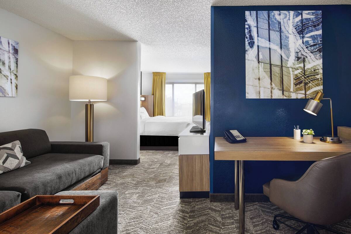 Une chambre d’hôtel avec un canapé, un bureau, une chaise, une lampe, un lit et un tableau au mur.