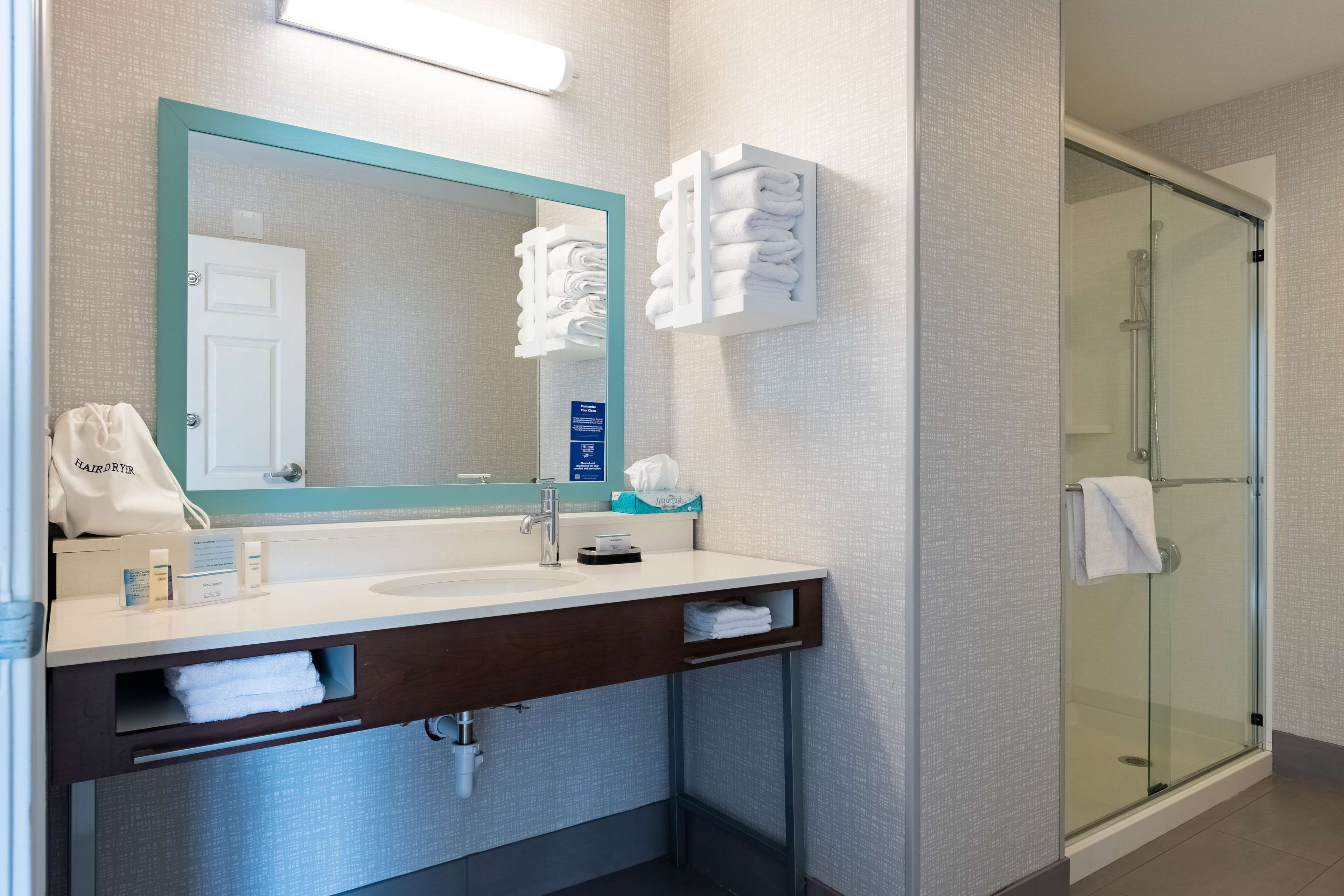 Un baño moderno con un espejo grande, un lavamanos, una cabina de ducha de vidrio y toallas dobladas con cuidado.