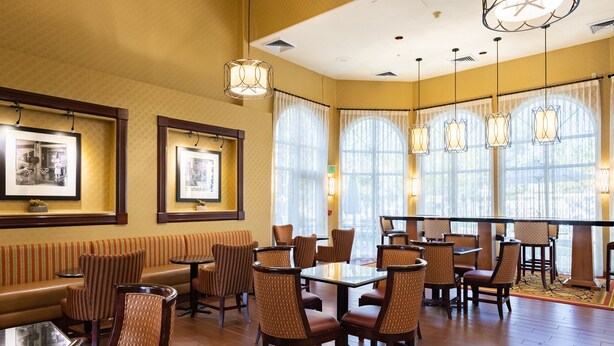 A restaurant with wooden flooring, cushioned seating, and pendant lighting. - Hampton Inn & Suites Salt Lake City Airport (Salt Lake City)