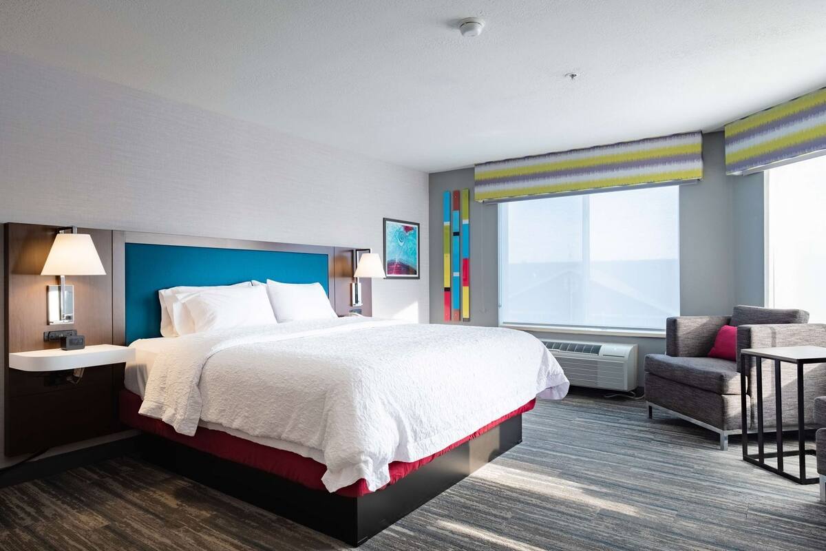 Ein modernes Hotelzimmer mit einem großen Bett, Nachttischen, einem Schreibtisch und einem Sessel.