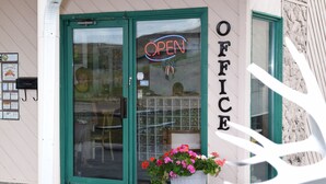 A storefront with a green door, a neon 'OPEN' sign, and a large potted plant with flowers.