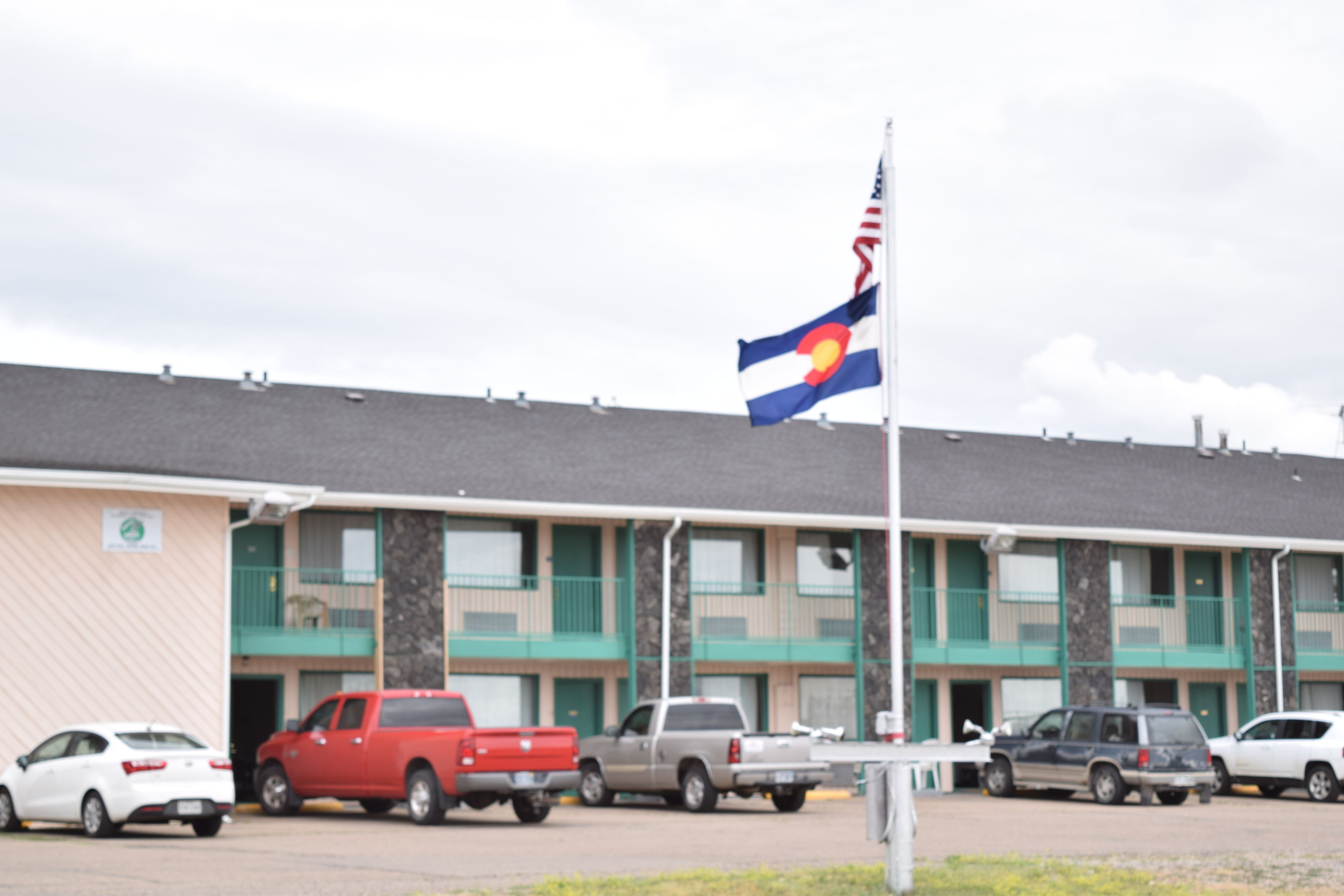 Un motel avec une rangée de voitures garées et un mât sur lequel flotte un drapeau.