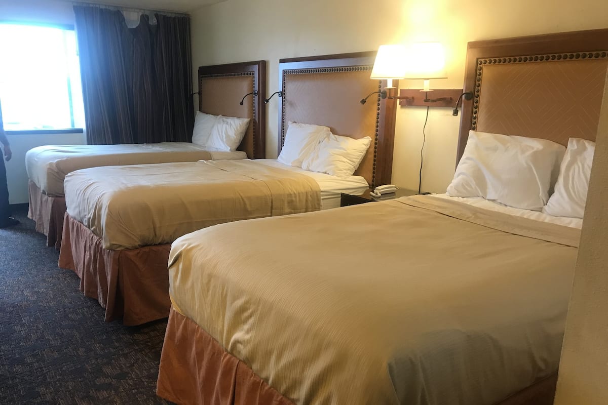 A hotel room with three beds, each with a wooden headboard and beige bedding.