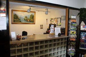 Un mostrador de recepción con un cuadro de paisaje enmarcado encima, un tablón de anuncios con varios avisos y una máquina expendedora de snacks.