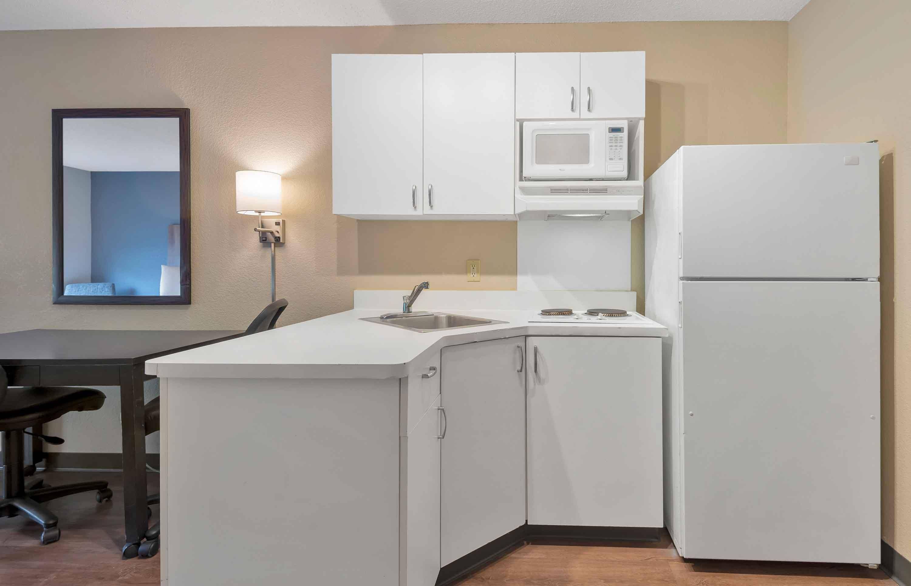 A compact kitchen with white cabinets, a microwave, a refrigerator, a sink, and a chair.