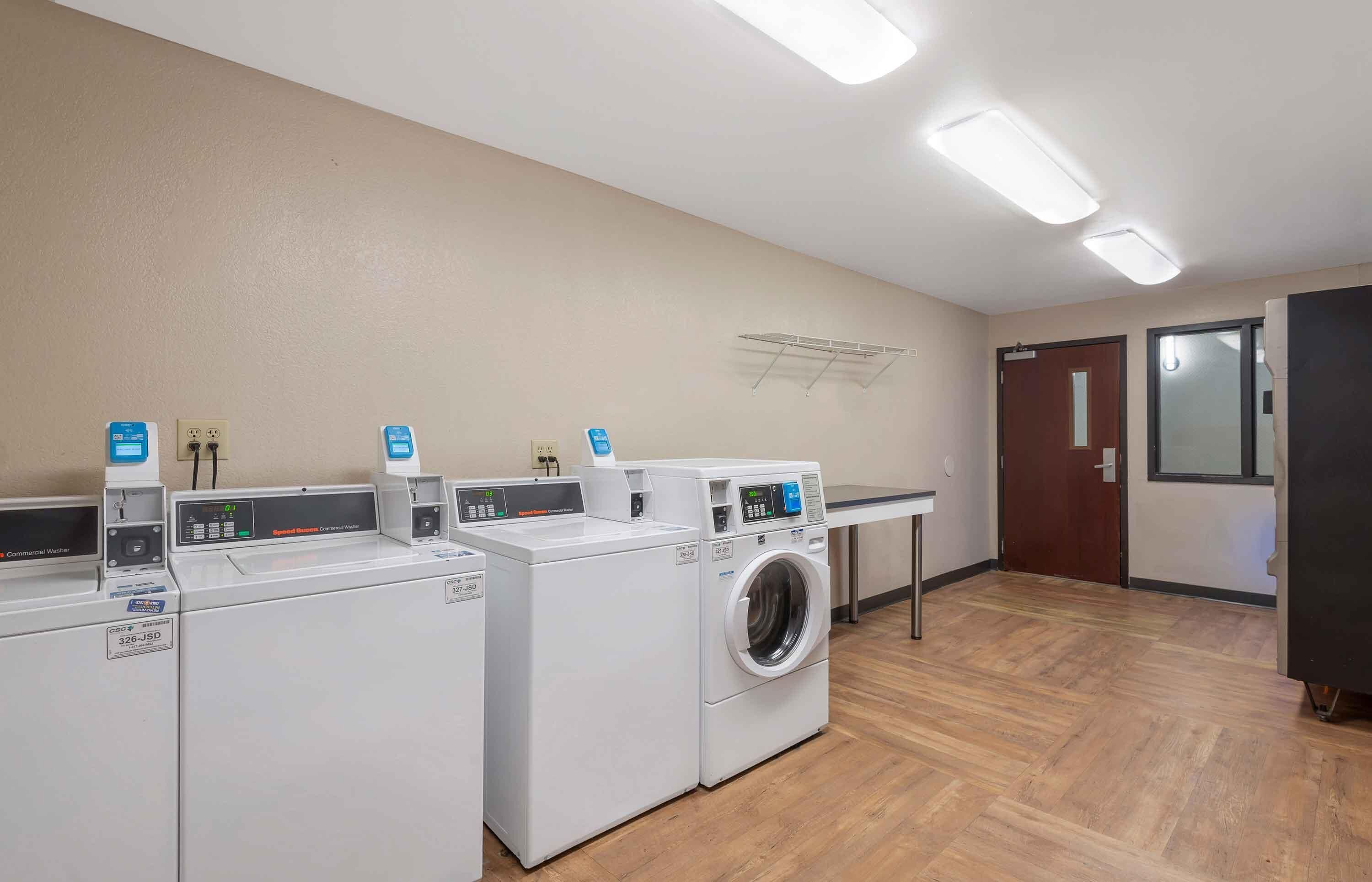 A laundry facility with multiple washing machines and dryers, a wooden floor, and a wall-mounted drying rack.