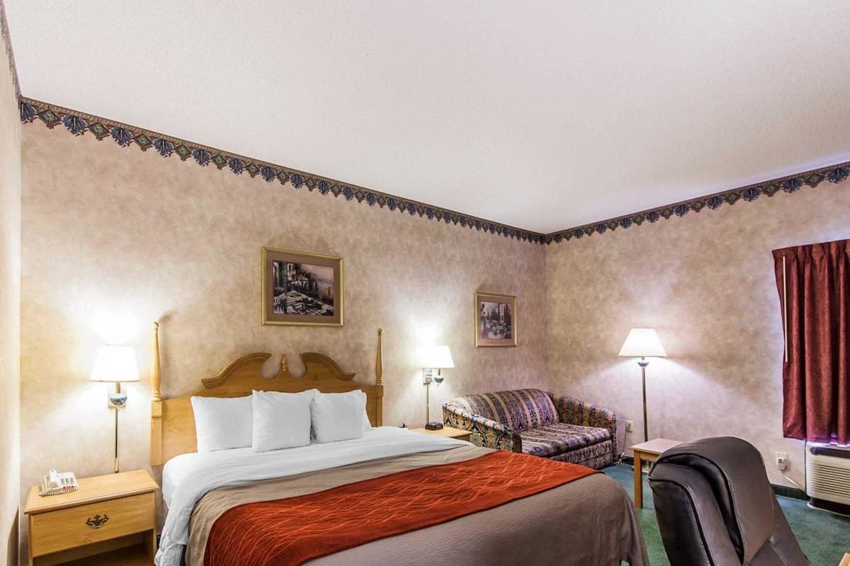 Habitación de hotel con una cama grande, dos mesitas de noche, una silla, un escritorio y dos lámparas.