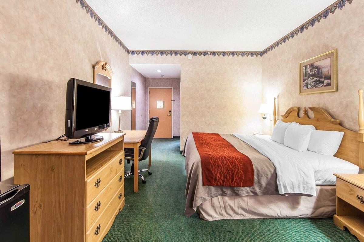Una habitación de hotel con una cama, un escritorio con computadora, un televisor y un aparador.