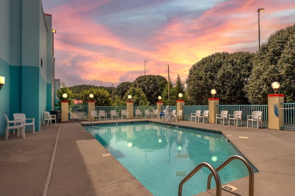 A swimming pool with lounge chairs and a sunset sky.