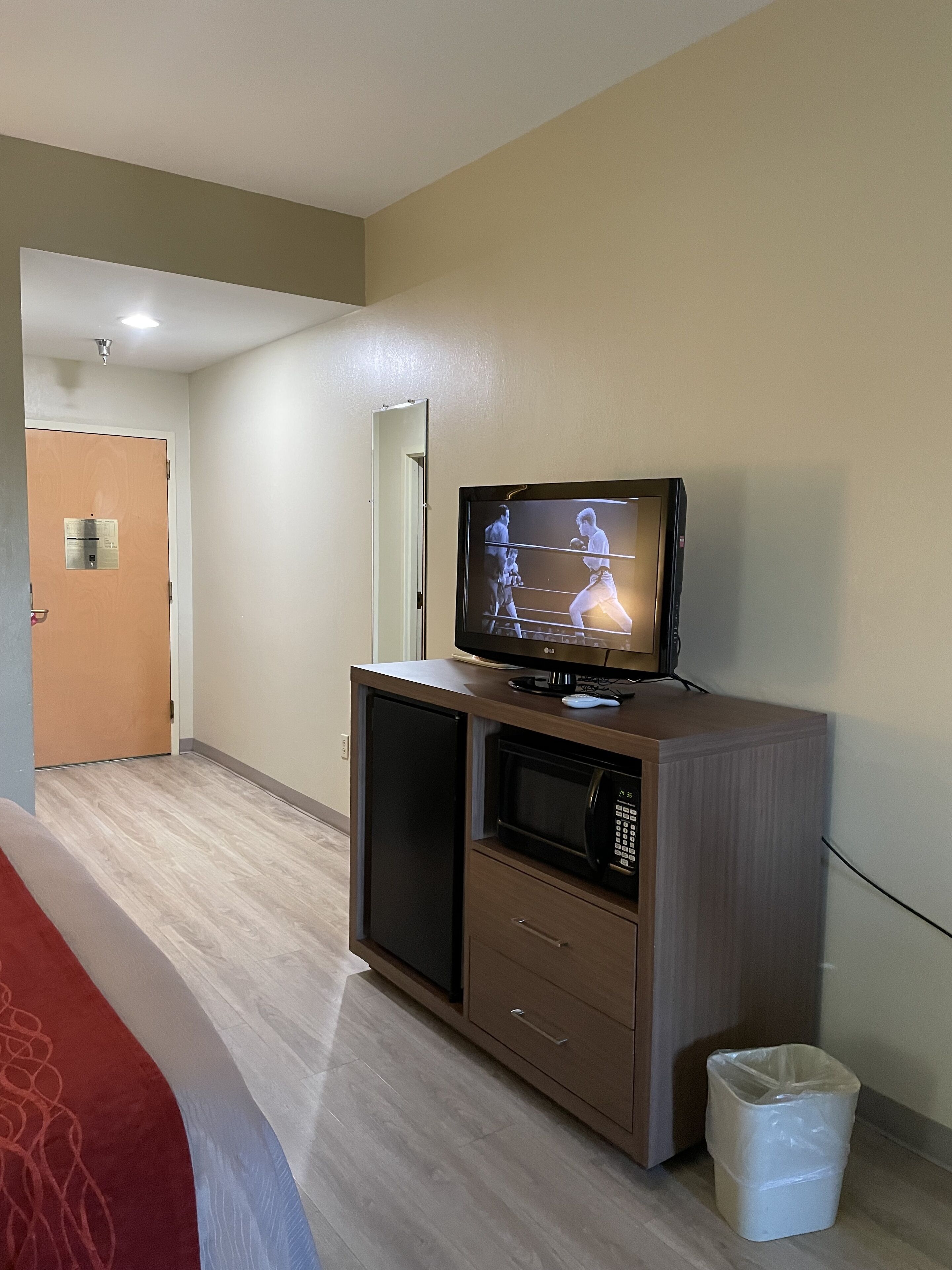 Habitación de hotel con televisión sobre un mueble de madera, un microondas y un cubo de basura.