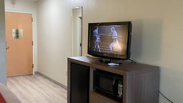 Habitación de hotel con televisión sobre un mueble de madera, un microondas y un cubo de basura.