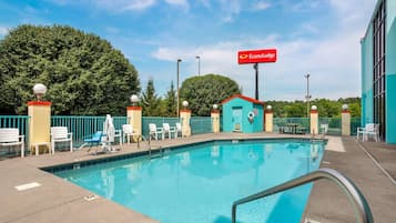 A swimming pool with lounge chairs and a lifeguard tower, surrounded by a fence and trees.
