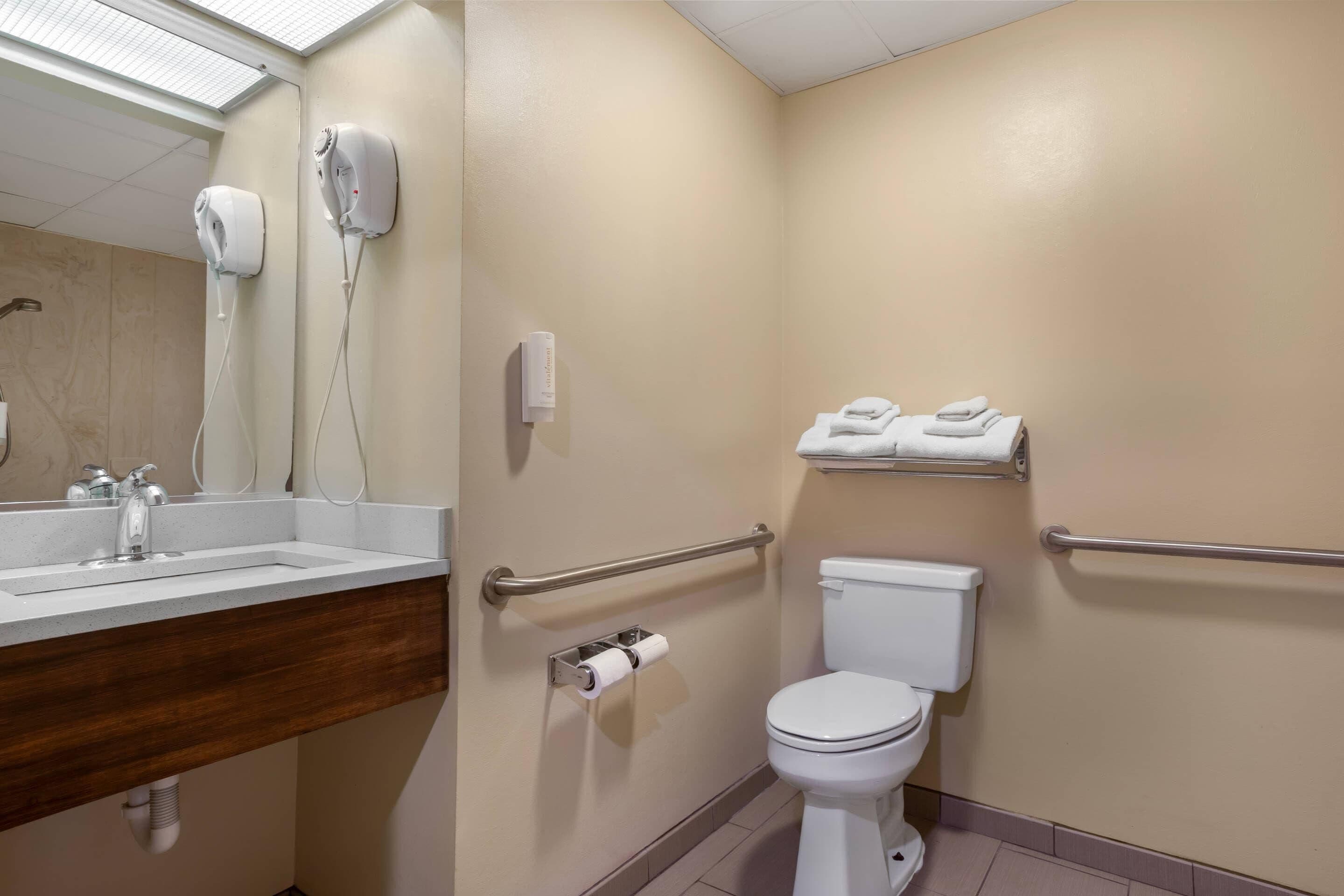 A bathroom with a sink, hand dryer, toilet, and towel rack.