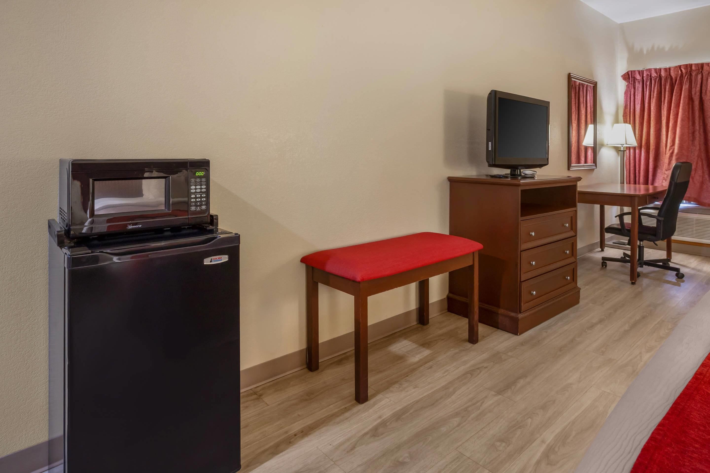 Une chambre d’hôtel équipée d’une kitchenette, d’un bureau avec une chaise, d’une télévision et d’une fenêtre avec des rideaux.