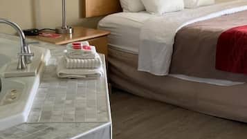 A hotel room with a wooden headboard, a bed with white linens, a marble bathroom sink, and two bedside lamps.