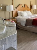A hotel room with a wooden headboard, a bed with white linens, a marble bathroom sink, and two bedside lamps.