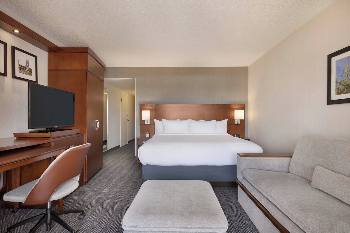 A hotel room with a bed, a desk with a chair, a television, and a sofa.