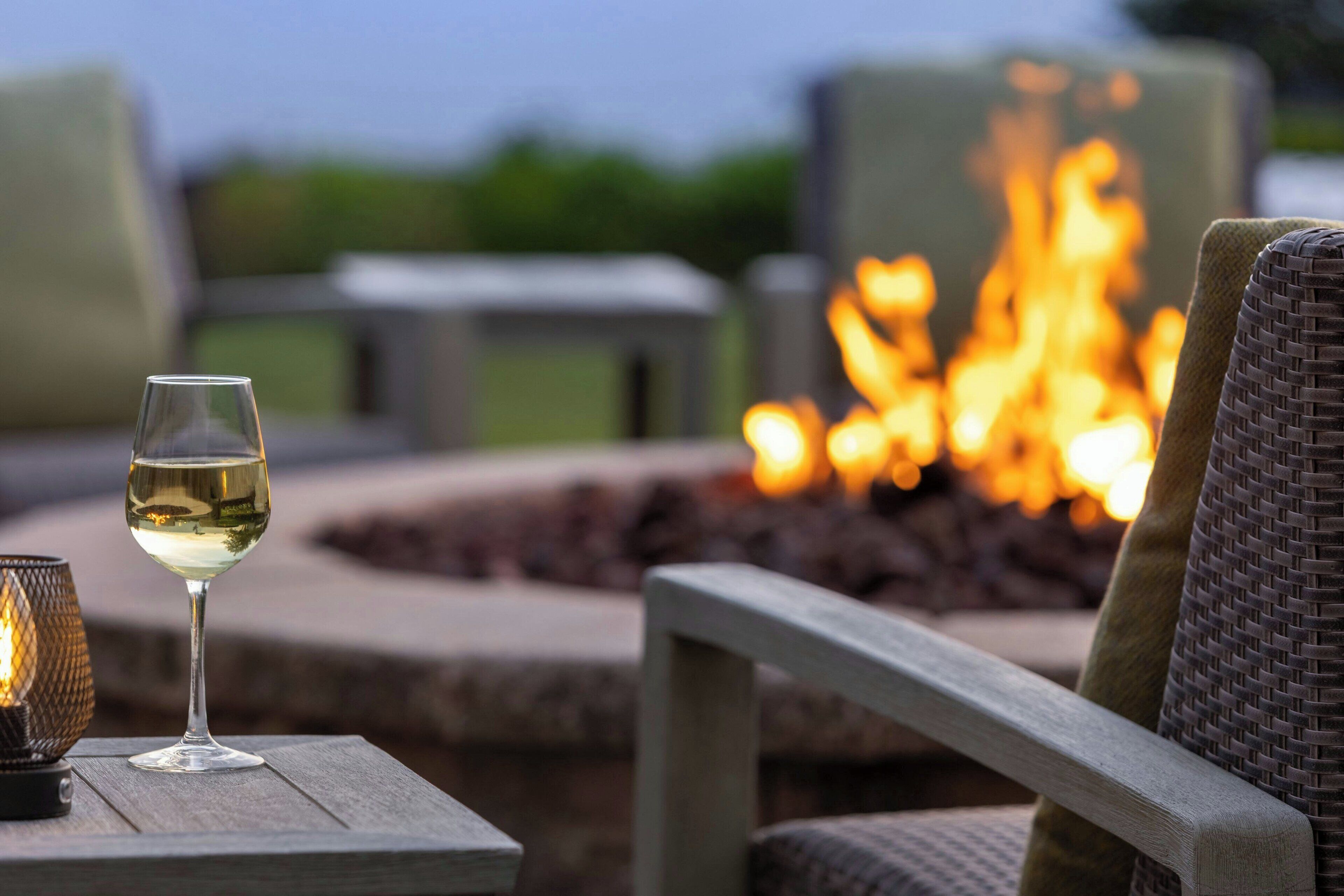 A glass of white wine on a wooden table with a fire pit in the background.