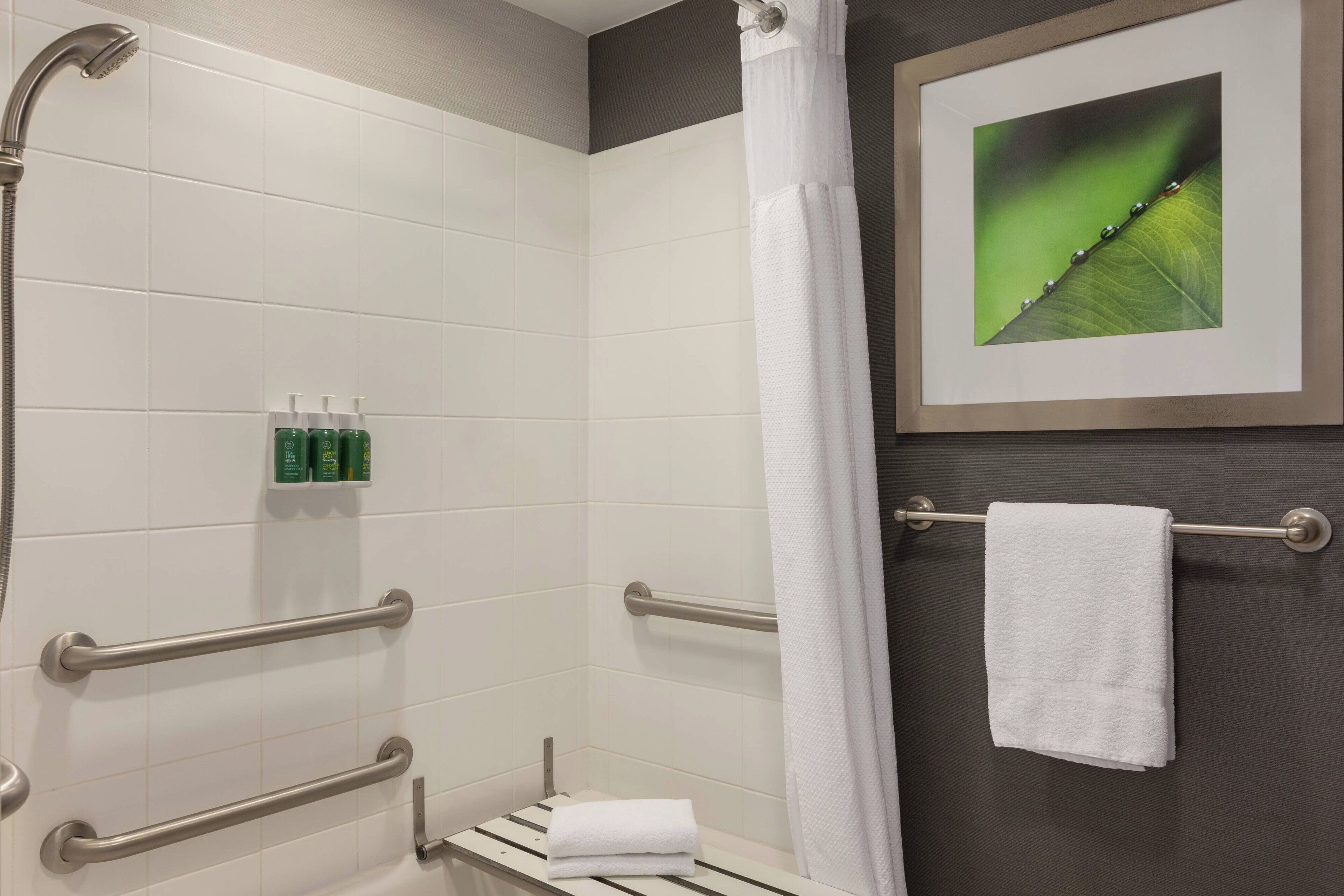 Ein modernes Badezimmer mit weißen Fliesen, einer Dusche inklusive Handbrause, einem Handtuchhalter mit einem weißen Handtuch und einem gerahmten Bild an der Wand.