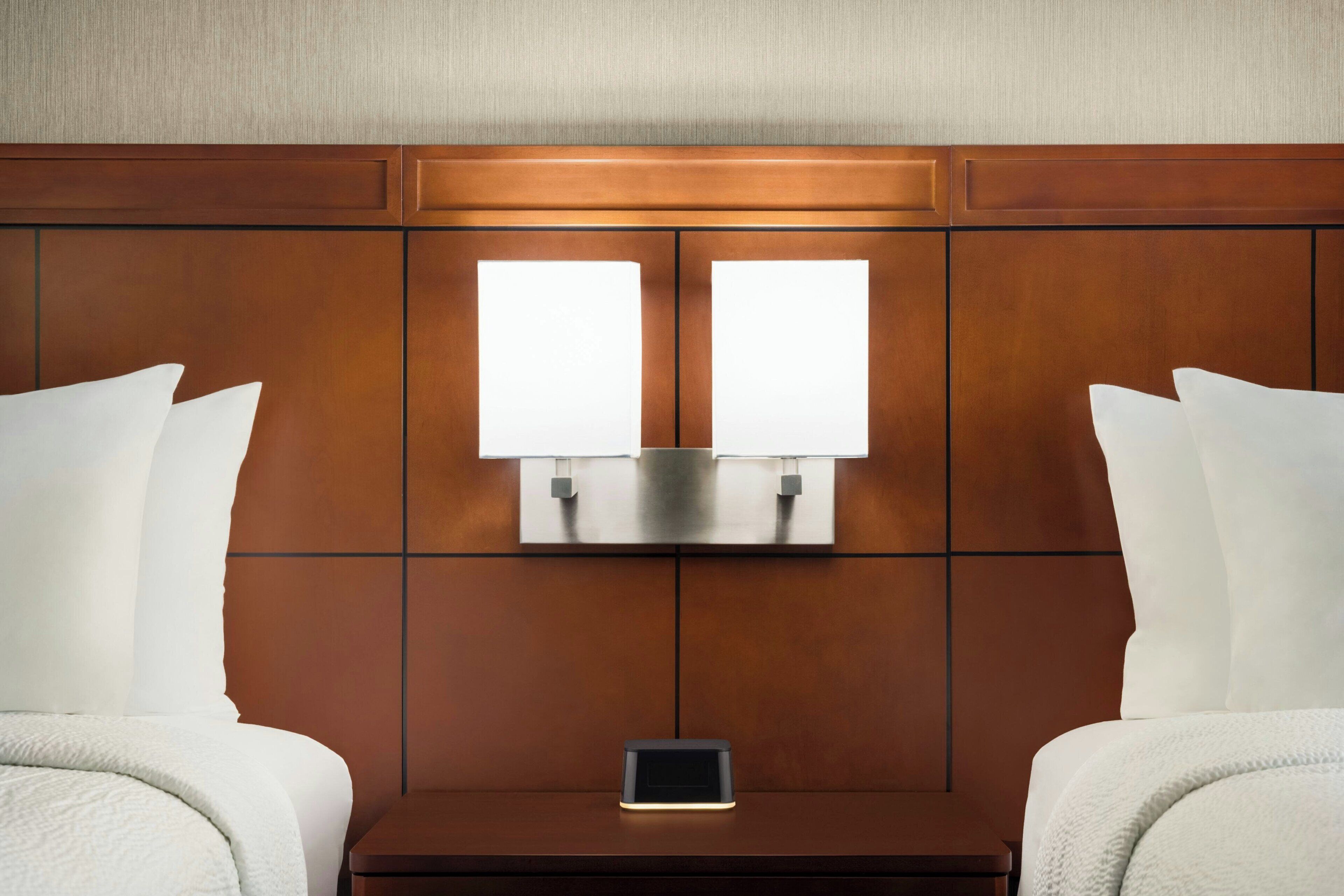 A hotel room with a wooden headboard, two bedside lamps, a nightstand, and a smartphone on the nightstand.