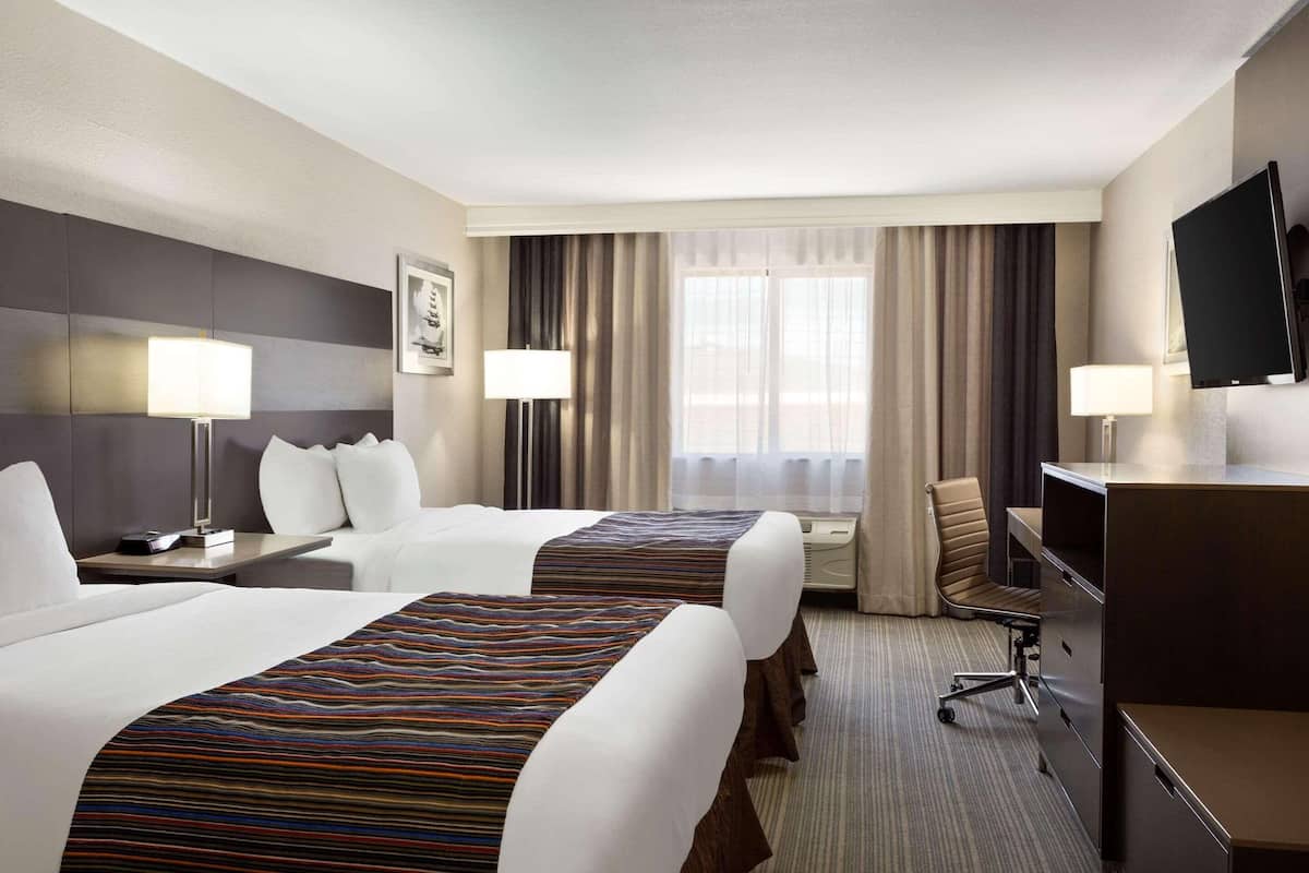 A hotel room with two beds, a desk, a chair, a TV, and a window with curtains.