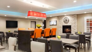 A modern dining area with a stone fireplace, orange chairs, and a flat-screen TV. - Country Inn & Suites by Radisson, San Antonio Lackland AFB - SeaWorld Area (San Antonio)
