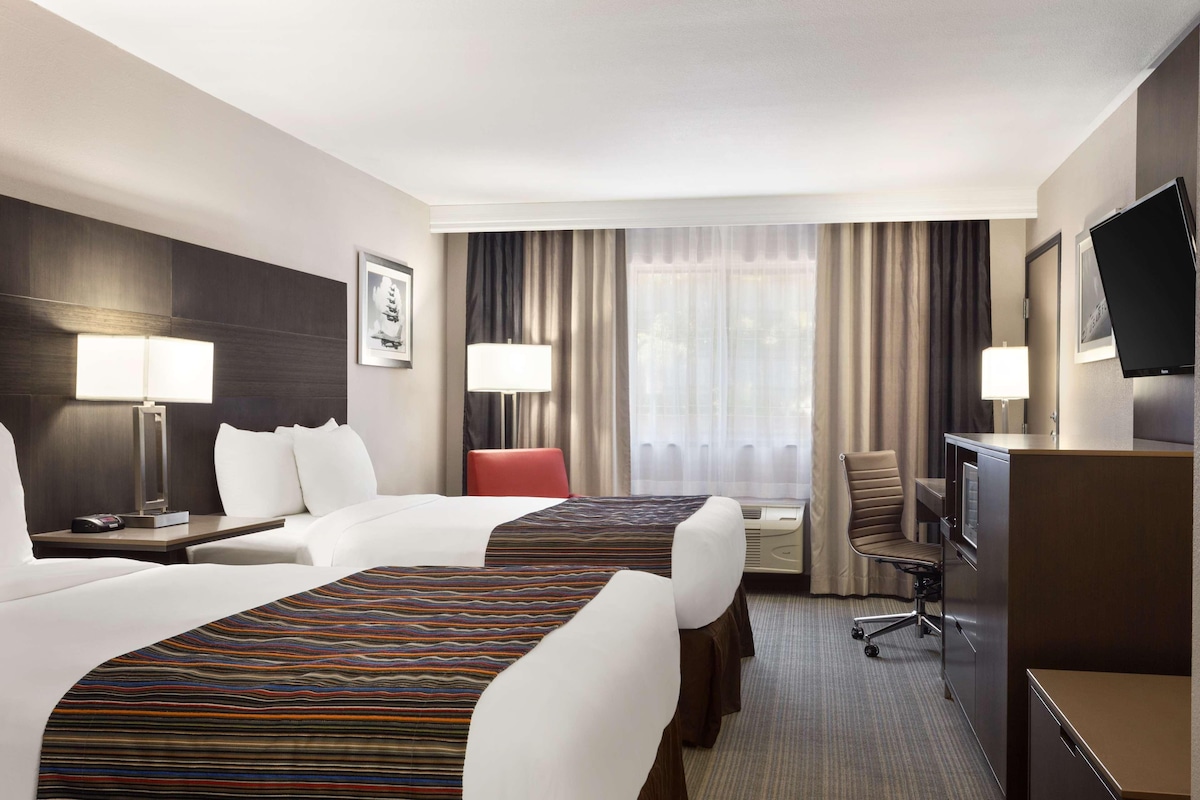 A hotel room with two beds, a desk, a chair, a TV, and a window with curtains.