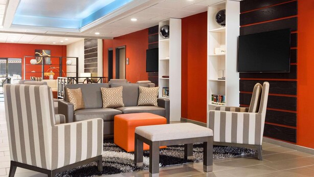 A modern living room with a sofa, two armchairs, a coffee table, and a flat-screen TV mounted on a black panel. - Country Inn & Suites by Radisson, San Antonio Lackland AFB - SeaWorld Area (San Antonio)