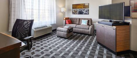 Habitación de hotel con sofá, reposapiés, televisor y escritorio.