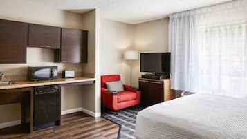 Une chambre d’hôtel avec une kitchenette, un fauteuil rouge, une télévision et un grand lit.