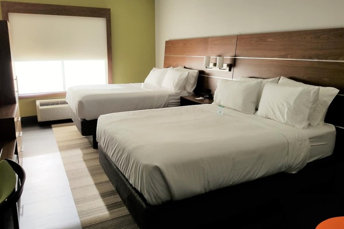 A hotel room with two beds, a nightstand, a chair, and a window with blinds.