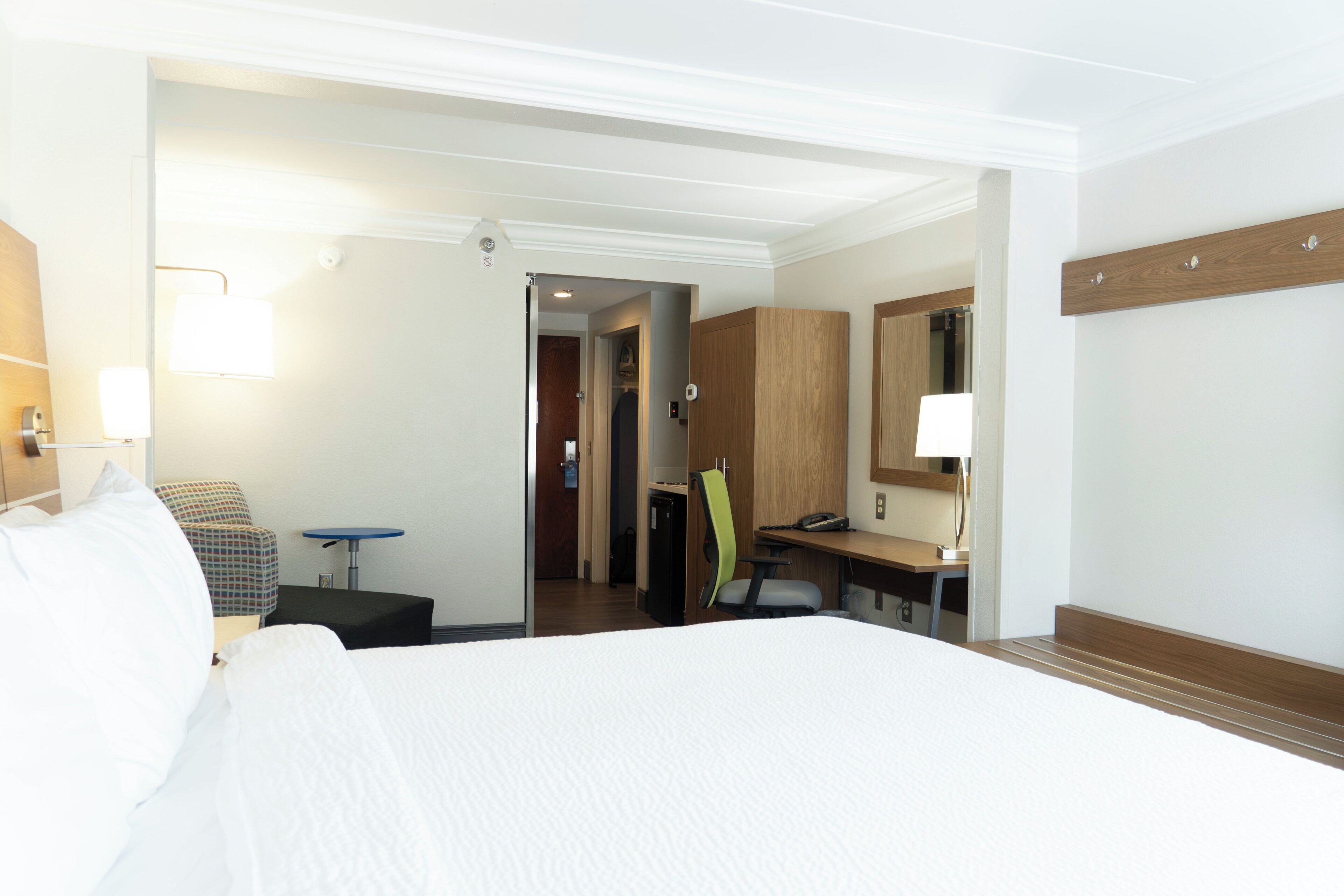 A hotel room with a large bed, a desk with a chair, a small table, and a mirror.