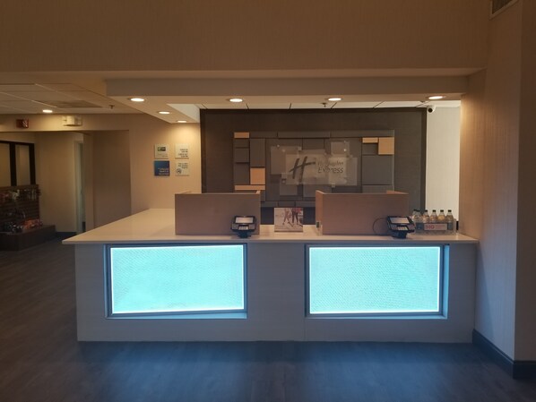 A hotel reception desk with two illuminated screens, a check-in counter, and a wall-mounted sign.