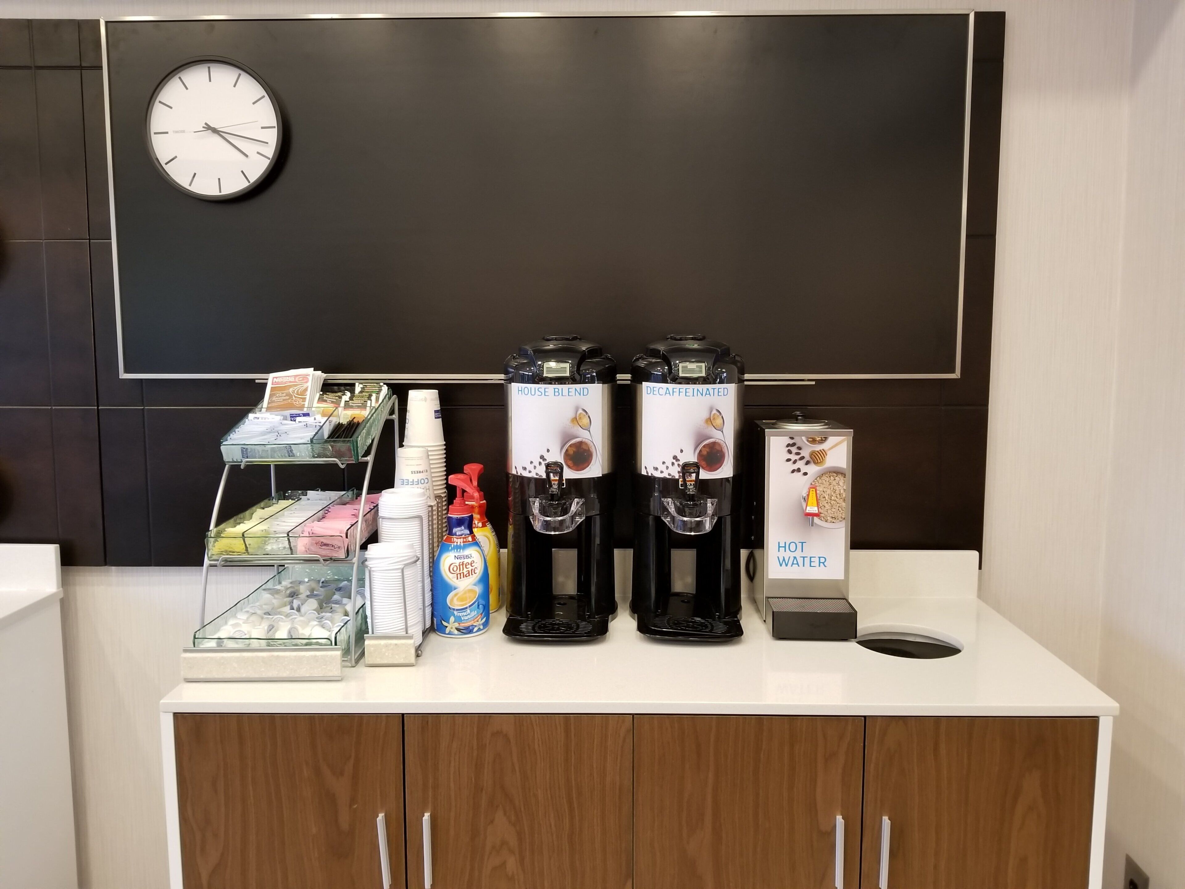 A coffee station with a clock, coffee machines, and a water dispenser.