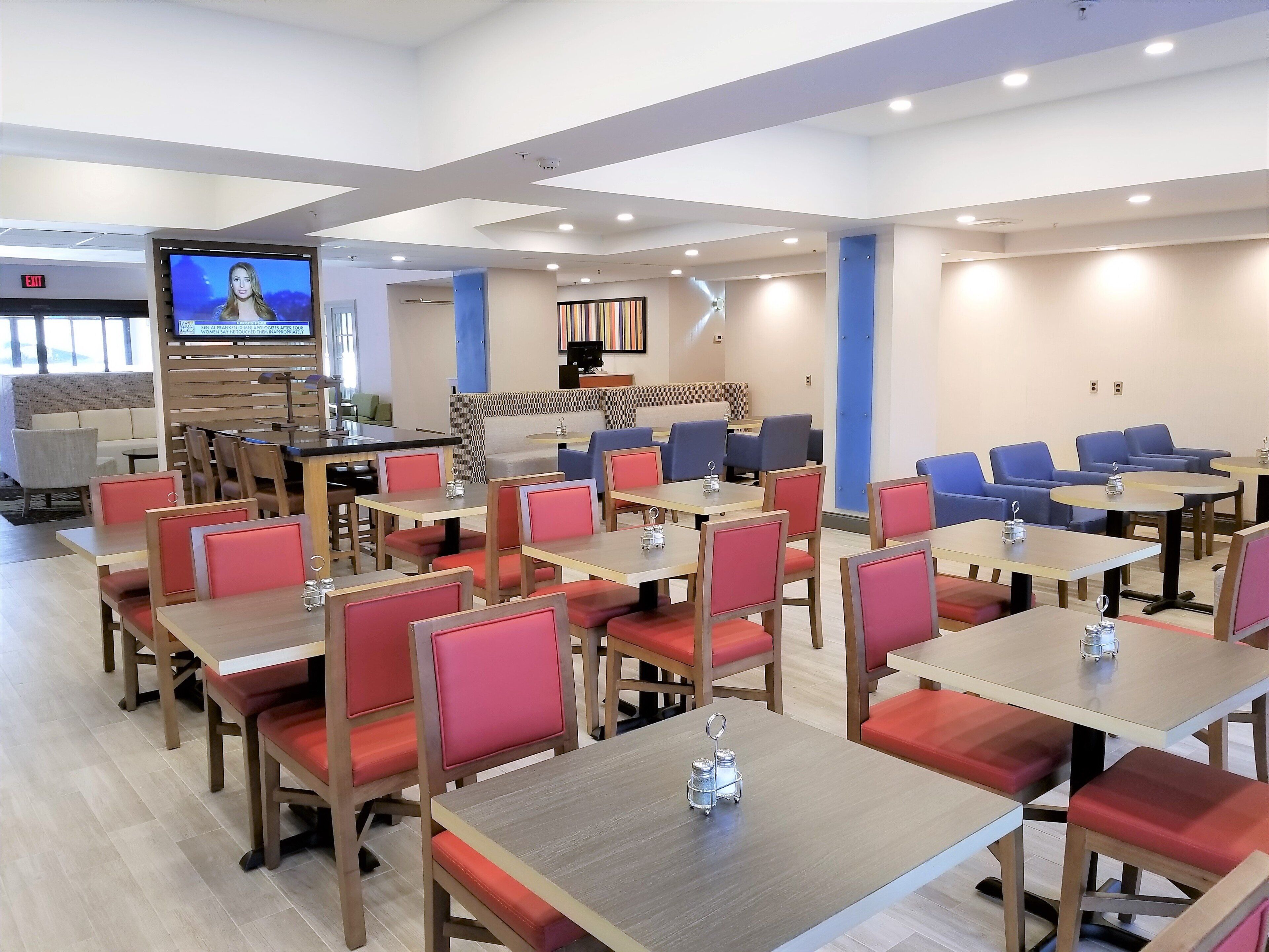Ein Hotelrestaurant mit mehreren Tischen und Stühlen, einem Fernsehbildschirm und einer Sitzecke mit Sofas und einer Theke.