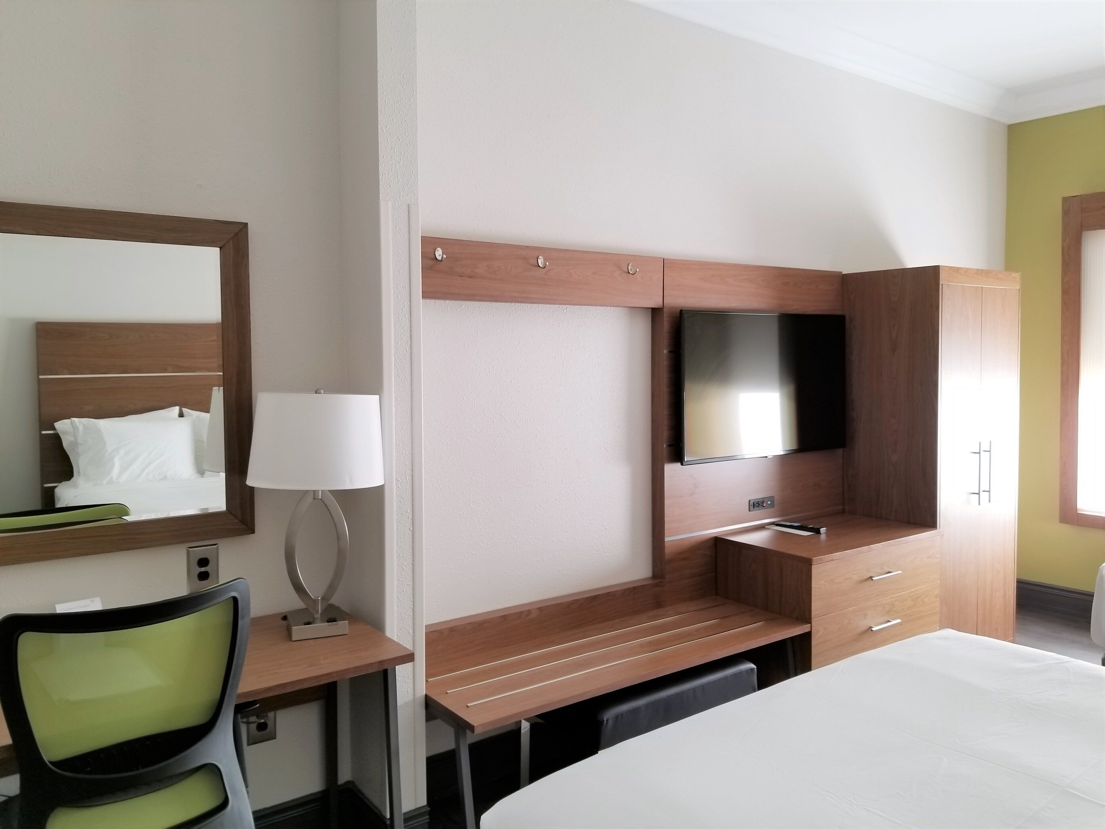 Una habitación de hotel con cama, escritorio, silla, televisor y armario.