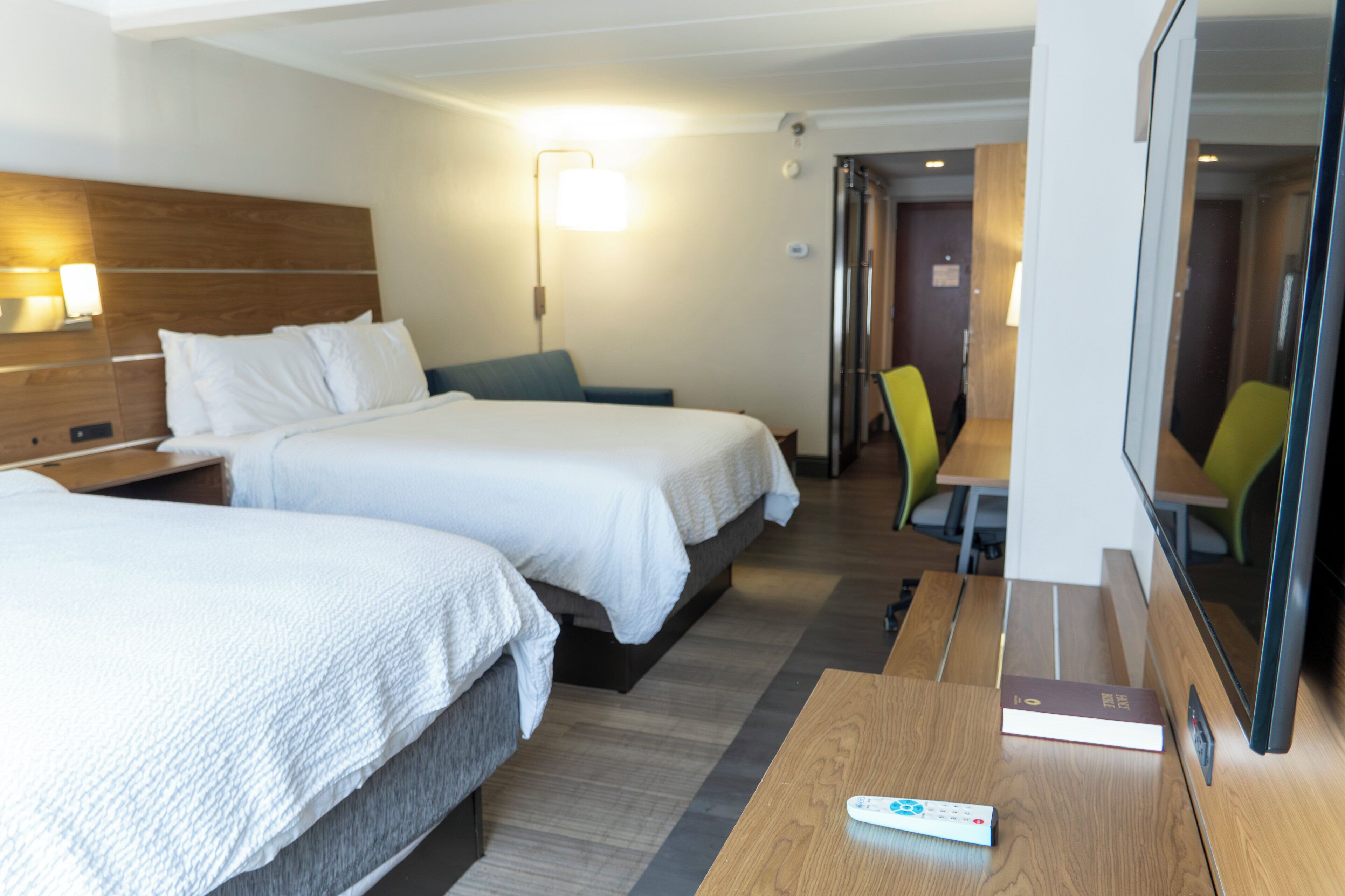 Quarto de hotel com duas camas, uma escrivaninha, uma cadeira e uma televisão.