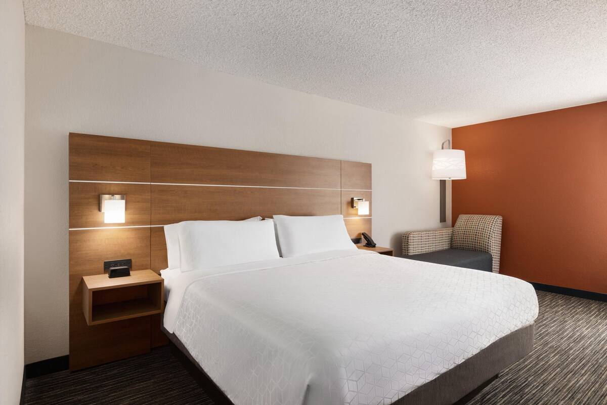 A hotel room with a large bed, bedside tables, a lamp, and a chair.