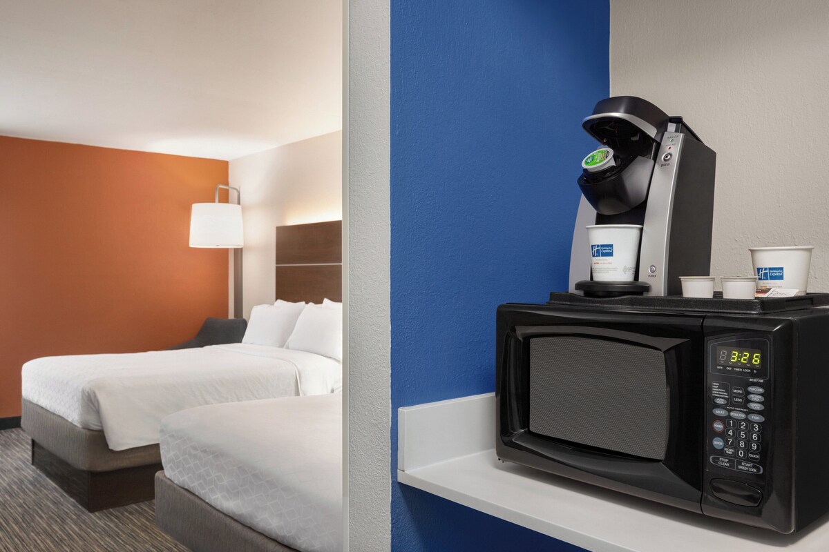 A hotel room with two beds, a microwave, a coffee machine, and a small table with cups.