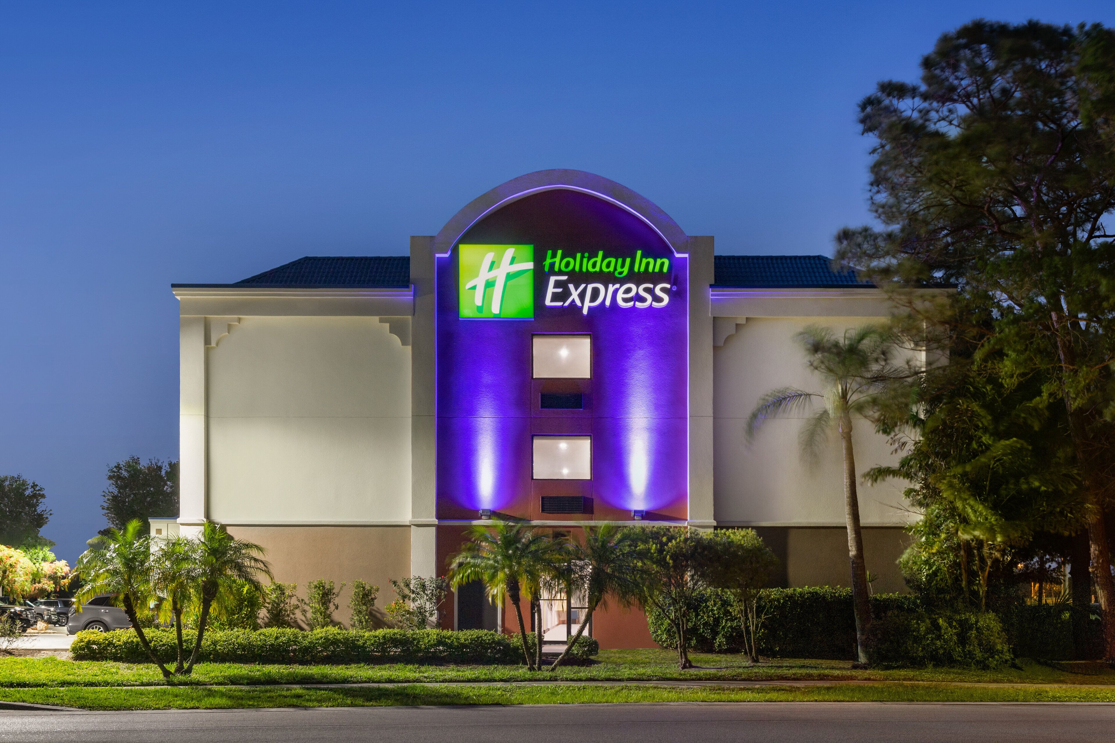 A Holiday Inn Express building with a prominent sign, surrounded by greenery and palm trees.