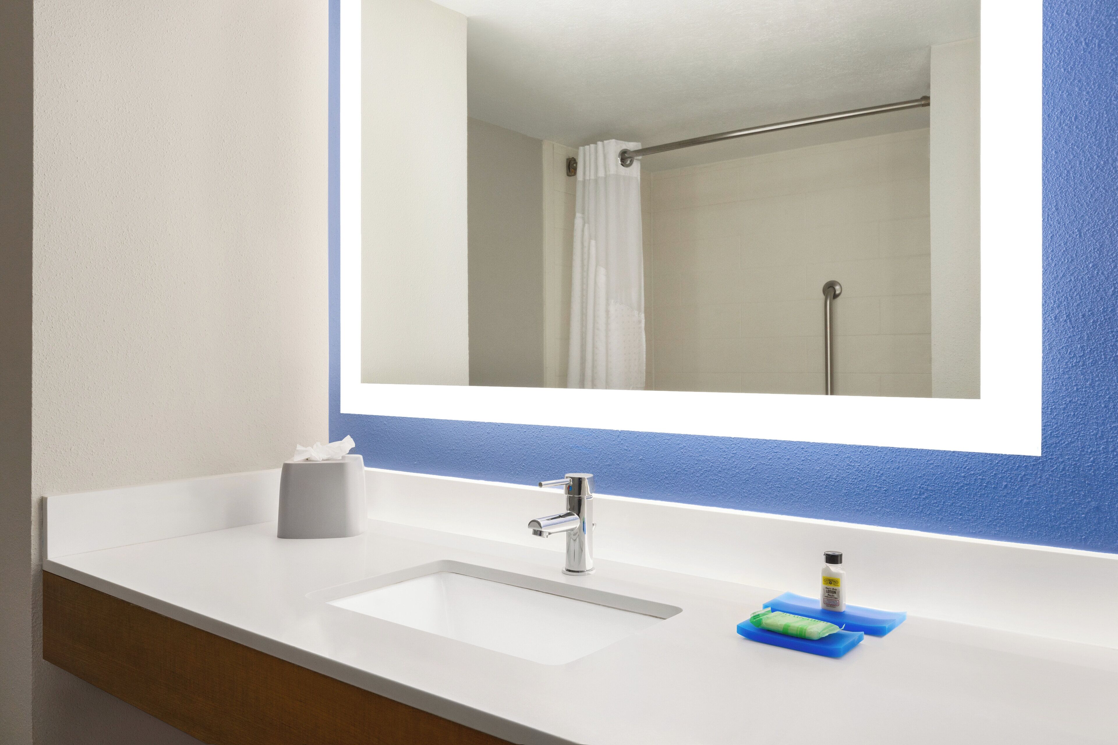 A bathroom with a white sink, a mirror, and a shower visible in the reflection.