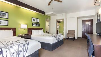 A hotel room with two beds, a desk, a chair, a television, and a ceiling fan.