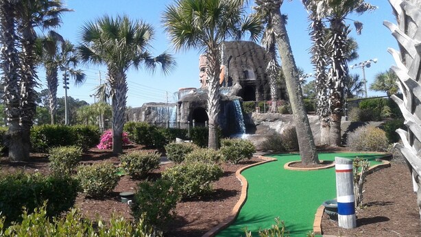 A miniature golf course with a green putting surface, palm trees, and a waterfall feature. - Sleep Inn Little River - North Myrtle Beach (Little River)