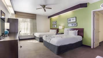 Une chambre d’hôtel avec deux lits, un bureau avec une lampe, un ventilateur de plafond et des tableaux encadrés au mur.