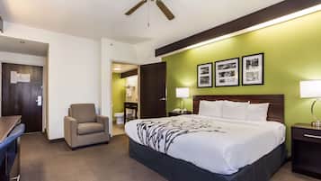 A hotel room with a bed, a desk, a chair, a nightstand, a lamp, and a ceiling fan.